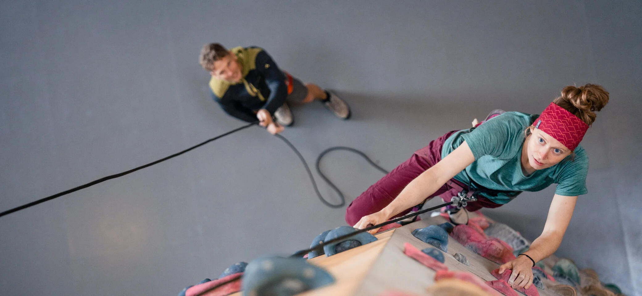 Eine Frau klettert in einer Kletterhalle, ihr Partner sichert sie. | © DAV / Julian Rohn